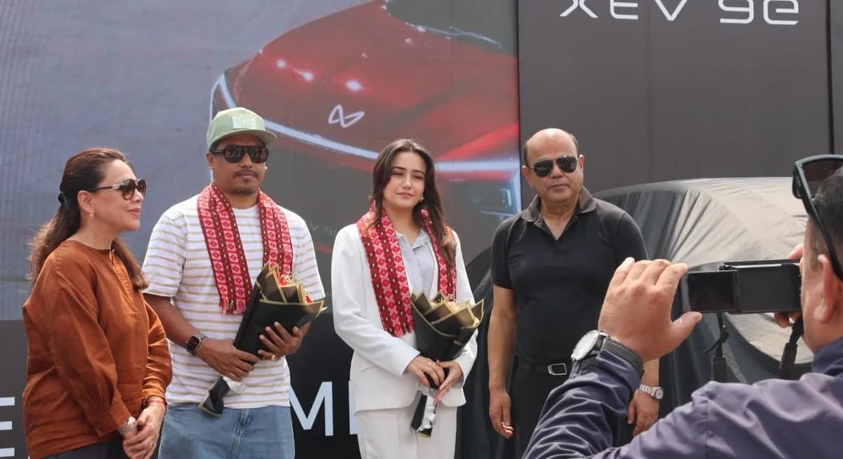 Cabinet Shrestha, right, with three guests holding bouquets at a launch in front of an XEV 9e screen