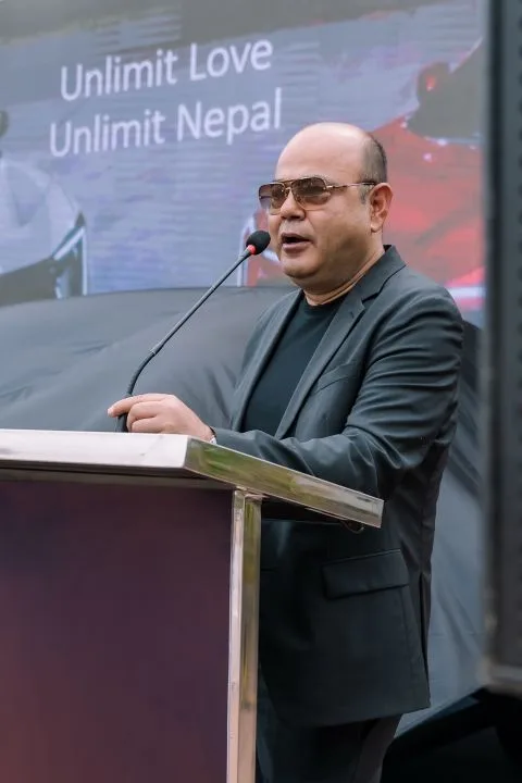 Cabinet Shrestha speaking at a podium in front of an “Unlimit Love, Unlimit Nepal” screen